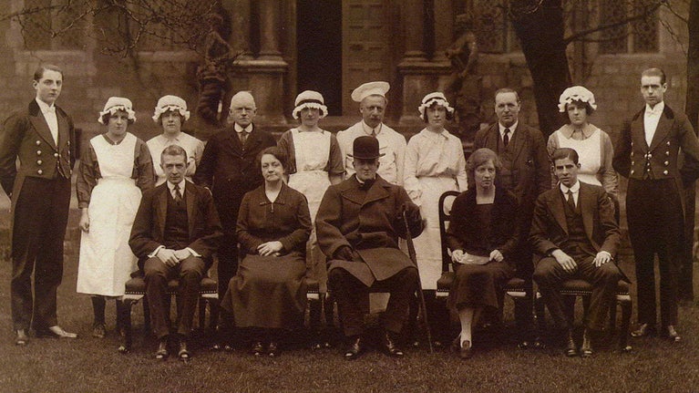 Smart man seated with two rows of staff in formal uniform